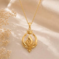Gold Plated Silver Empress Flame Crest Necklace with a crowned openwork flame pendant on champagne satin beside dried flowers