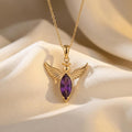 Gold Plated Silver Angel Wing Necklace with feather-detailed wings and a purple marquise-shaped center stone on ivory fabric