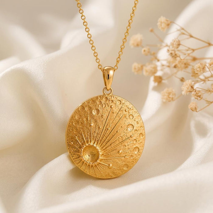Gold Plated Silver Lunar Impact Pendant front view with crater texture and radiating lines on ivory satin beside dried flowers