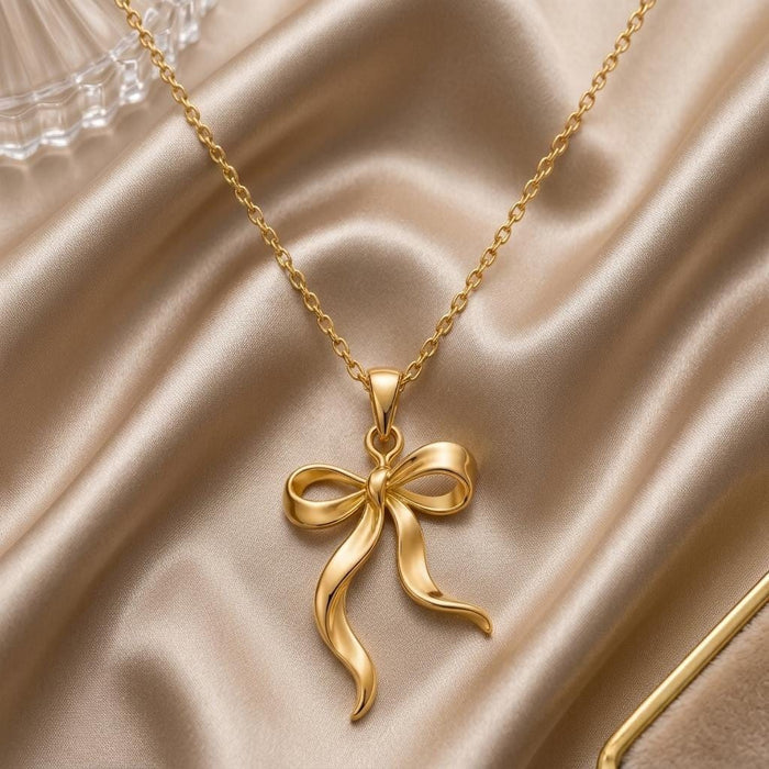 Gold Plated Silver Ribbon Flow Necklace with an open ribbon bow and long asymmetrical tails on champagne satin