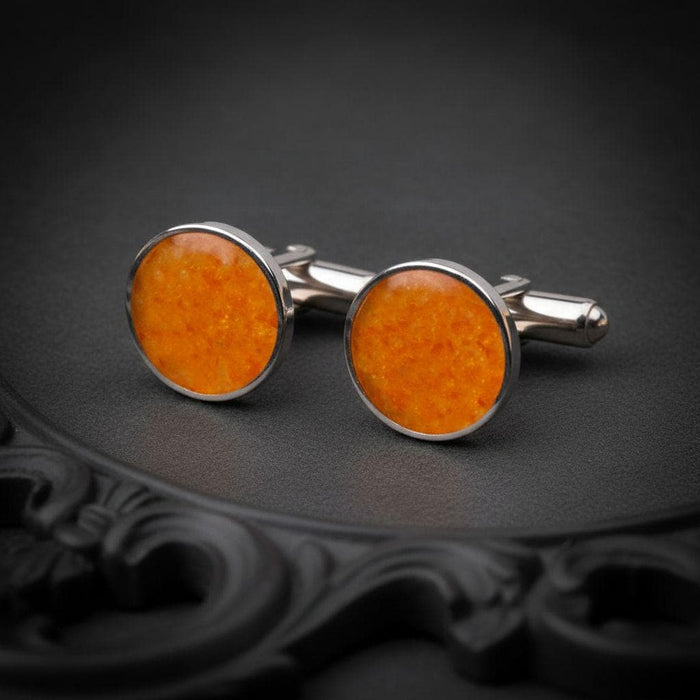 Pair of round amber stone cufflinks with orange-toned faces and cylindrical backs on a dark ornamental tray