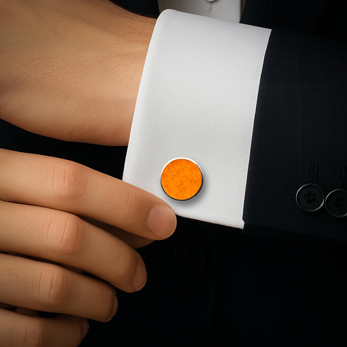 Round amber stone cufflink worn on a white dress-shirt cuff beneath a dark tailored jacket