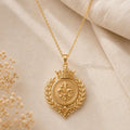 Gold Plated Silver Royal Laurel Sigil Pendant with a crowned fleur-de-lis and laurel branches on a neutral textured surface
