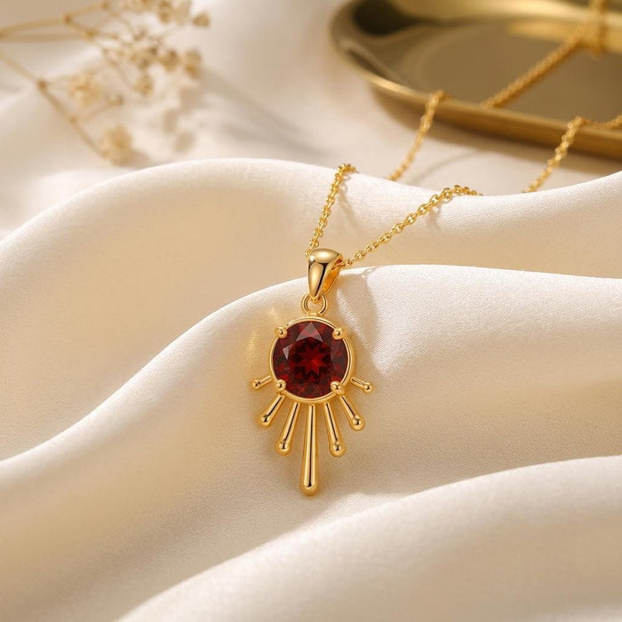 Gold Plated Silver Sun Drop Pendant Necklace with deep red center on ivory satin beside a tray