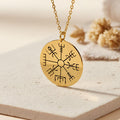 Gold Plated Silver Vegvisir Compass Necklace with a closed round engraved eight-arm compass pendant on a light stone surface