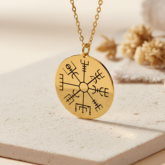 Gold Plated Silver Vegvisir Compass Necklace with a closed round engraved eight-arm compass pendant on a light stone surface